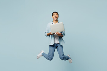 Full body young IT man of African American ethnicity he wearing shirt casual clothes jump high hold use work on laptop pc computer isolated on plain pastel light blue cyan background studio portrait.