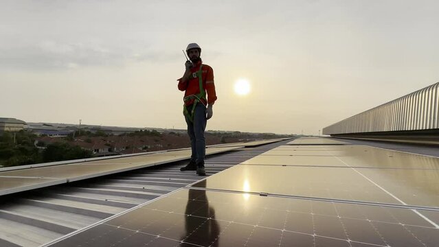 A technician sits on a rooftop, examining solar panels under a clear blue sky. He points while taking notes, ensuring everything is functioning properly.