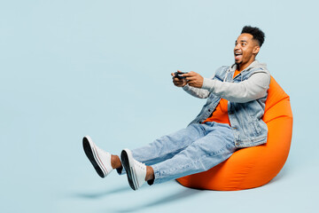 Full body young man of African American ethnicity wear denim jacket orange t-shirt sit in bag chair...