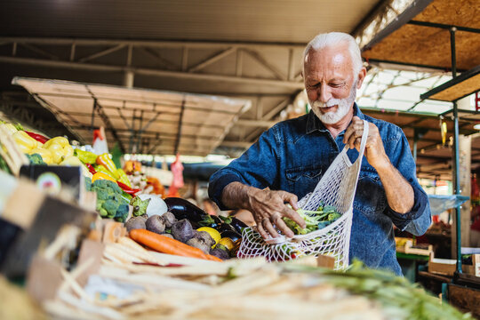 Cheerful senior man selecting fresh vegetables in market, everything is fresh and organic. Healthy food for healthy life.