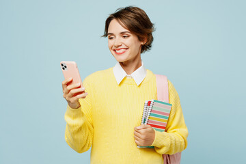 Young smiling woman student wear casual clothes yellow sweater backpack bag hold books use mobile...