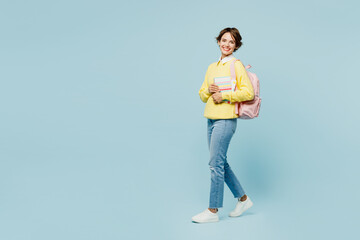 Fototapeta na wymiar Full body side profile view young woman student wear casual clothes sweater backpack bag hold books look camera walk go stroll isolated on plain blue background High school university college concept