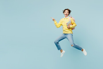 Obraz premium Full body young woman student wear casual clothes sweater hold backpack bag jump high run fast hold books point finger aside isolated on plain blue background. High school university college concept.
