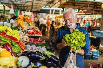 Eldery man buying vegetables at the market. Senior man buys organic vegetables at the market.