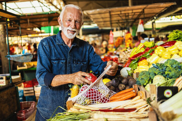 Man choosing fruits and vegetables on the farmer's market. Mature man buying vegetables at the market. A man shops in a local outdoor agriculture market with fresh, organic local fruits and vegetables