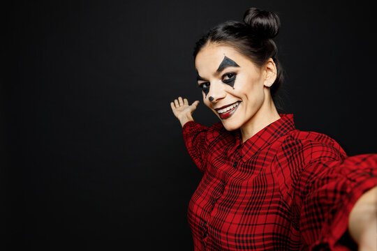 Young woman with Halloween makeup face art mask wears clown costume red dress do selfie shot on mobile cell phone isolated on plain solid black background studio portrait. Scary holiday party concept.