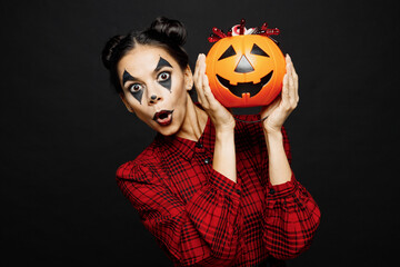 Young shocked fun woman with Halloween makeup face art mask wear clown costume red dress hold Jack-o-Lantern carved pumpkin isolated on plain solid black background studio Scary holiday party concept