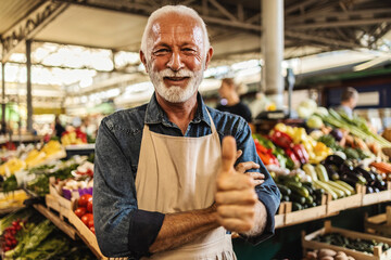 An Caucasian senior vegetable stall owner portrait looking at camera smiling.