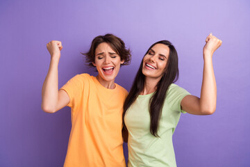 Photo of cheerful lucky ladies wear t-shirts hugging screaming yes rising fists isolated violet color background