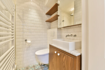a small bathroom with white tiles and wood cabinetd vanity in the corner, there is a mirror on the wall