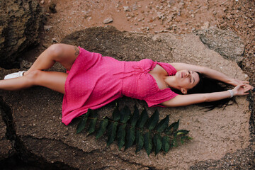 Beautiful woman in pink dress lying on a big stone at seashore