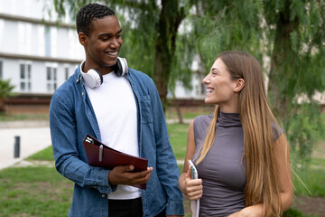 Multiracial couple smiling and holding folders in a campus.Two young students looking each other...