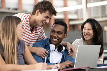 Multicultural group of people working together with a laptop.Young happy friends laughing outside using computer and notes.
