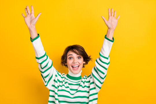 Photo of excited funky girl dressed striped sweater rising arms waving isolated yellow color background