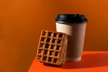 Waffle and hot cup of coffee on orange background.