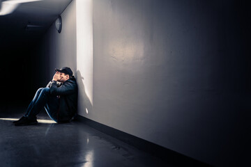 Sad man with trauma sitting on floor. Shame, guilt or sorrow. Desperate guy crying in dark corridor. Victim of loneliness or discrimination. Negative emotion or depression. Lonely outcast worrying. - obrazy, fototapety, plakaty