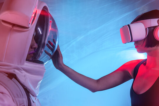 Anonymous astronaut in spacesuit and woman wearing VR goggles