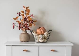 Autumn decor on the dresser in the living room - a bouquet of autumn leaves and berries and a...