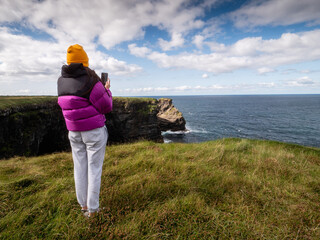 Young teenager blogger filming stunning nature scene on her smart phone. Ireland, Kilkee area....