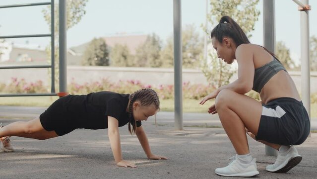 Asian woman trainer watching a kid girl doing push-ups from the ground, warm-up training. Boxing training for children on the outdoor training ground