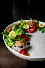 chef or waiter hold plate with Salad nicoise. Tuna, with green beans, tomatoes, potatoes and a vinaigrette mustard dressing