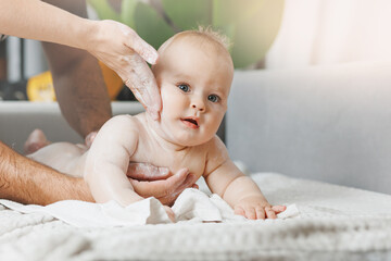 Mother and father applying body cream on her little baby son at home
