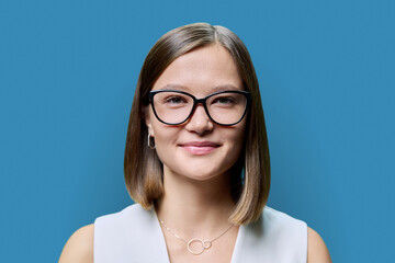 Fototapeta premium Headshot portrait of young beautiful woman in glasses, on blue studio background