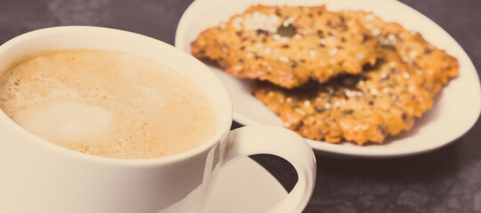 Cup of coffee with milk and fresh baked oatmeal cookies on white plate. Delicious crunchy dessert