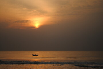 A Fishing boat approaching shore with catch fish carrying the fisherman during the sun raise with golden sun at the background with selective focus