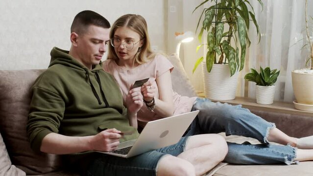 Happy online retail web services buyers make easy purchase, instant money transfer, use secure remote e payment concept. Couple in love sit on sofa with laptop holding credit card buying on internet