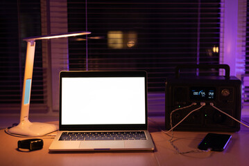 Charging station for laptop and desk lamp when there is no light during blackout. Generator power bank battery in the absence of electricity. at home table - obrazy, fototapety, plakaty