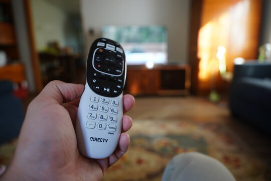 DirectTV remote control is being held while watching subscription cable television.  