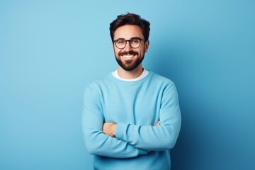 Young handsome man with beard wearing casual sweater and glasses over blue background happy face smiling with crossed arms