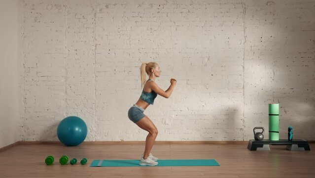 Healthcare and wellness advertisement concept. Athletic woman fitness coach doing classic squats for online classes, side view.