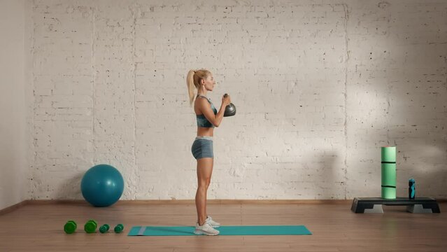 Healthcare wellness advertisement concept. Athletic woman fitness coach doing kettlebell squats for online classes, side view.