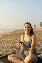 Fototapeta na wymiar beautiful young lady smiling to the camera holding her smartphone after exercising. technology concept