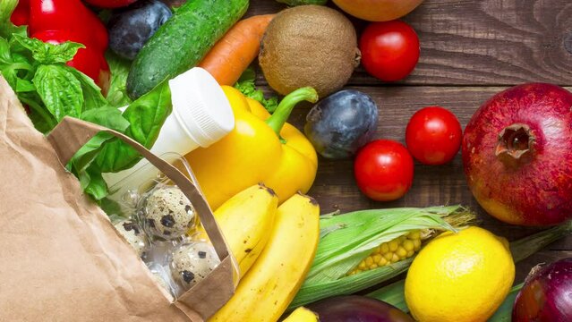 Full paper bag of different healthy diet food on rustic wooden background. Fruits, vegetables, eggs, bread and milk. Top view