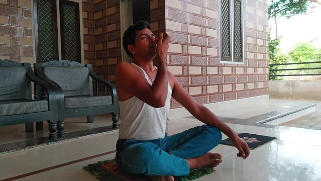 Indian man doing nostril breathing or pranayama yoga by closing eyes during morning at home concept of healthy lifestyle, wellness and mindfulness
