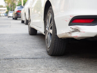 Close up of the rear bumper dent of a white sedan car park on the concrete road - obrazy, fototapety, plakaty