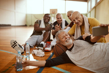 Diverse group of male senior friends taking selfies after playing basketball in a indoor gym - Powered by Adobe
