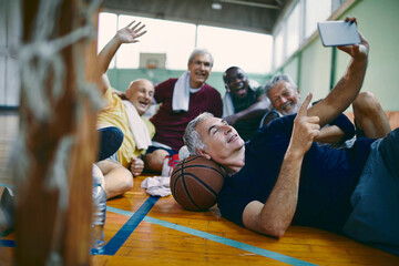Diverse group of male senior friends taking selfies after playing basketball in a indoor gym