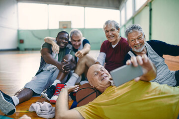 Diverse group of male senior friends taking selfies after playing basketball in a indoor gym