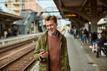 Middle aged man using his smartphone while waiting for the train at the train station
