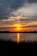 Orange summer sunset  with clouds, God's rays and trees in silhouette at North Turtle Lake in Minnesota, USA
