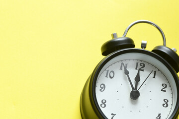 Black alarm clock on a yellow background.
