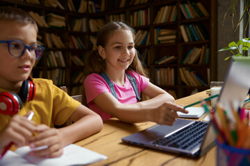 Little schoolchildren studying together using laptop