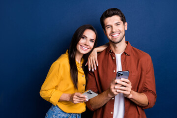 Portrait of two positive idyllic partners embrace toothy smile use smart phone isolated on dark blue color background