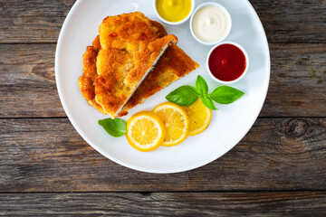 Crispy breaded seared chicken cutlet with lemon slices and fresh vegetables on wooden table

