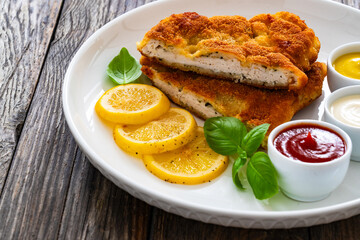 Crispy breaded seared chicken cutlet with lemon slices and fresh vegetables on wooden table
