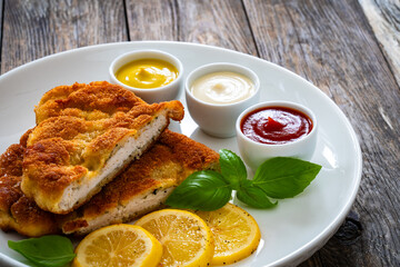 Crispy breaded seared chicken cutlet with lemon slices and fresh vegetables on wooden table

